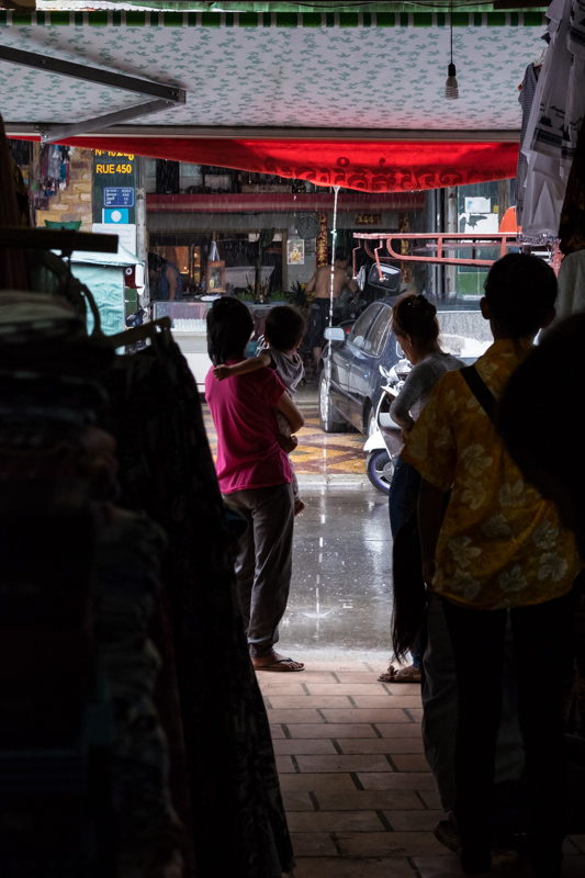 mother child and father wait at the side of the market for the rain to fade