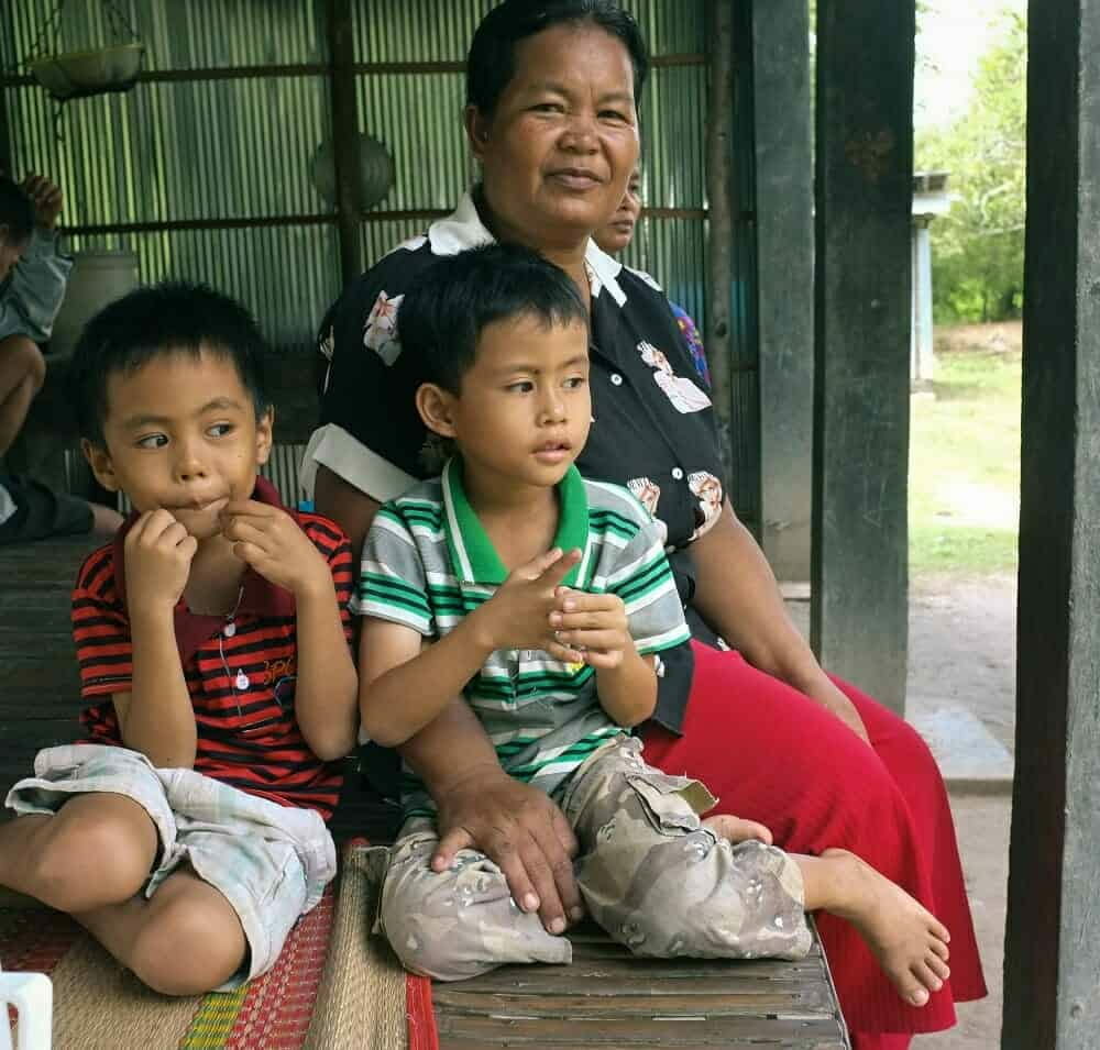 two boys look at the camera while sitting in their foster mum's legs